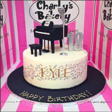 Single tier 18th birthday cake iced white chocolate ganache, decorated 3D Grand Piano and piano stool topper, 3D microphone topper, swoosh of piped musical notes